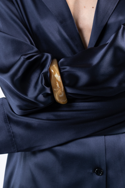 Dettaglio della camicia oversize in satin di seta blu. L'immagine evidenzia il rever ispirato alla giacca, il drappeggio morbido delle maniche e la lucentezza naturale del tessuto.